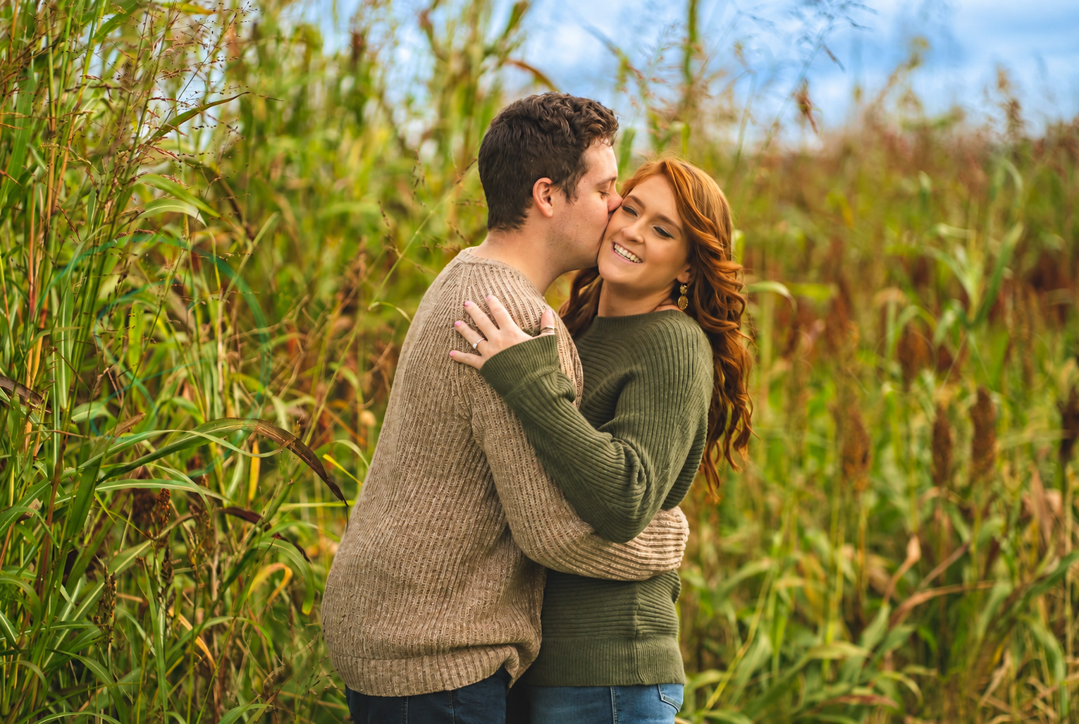 A couple embracing in tall grass and sharing a kiss on the cheek