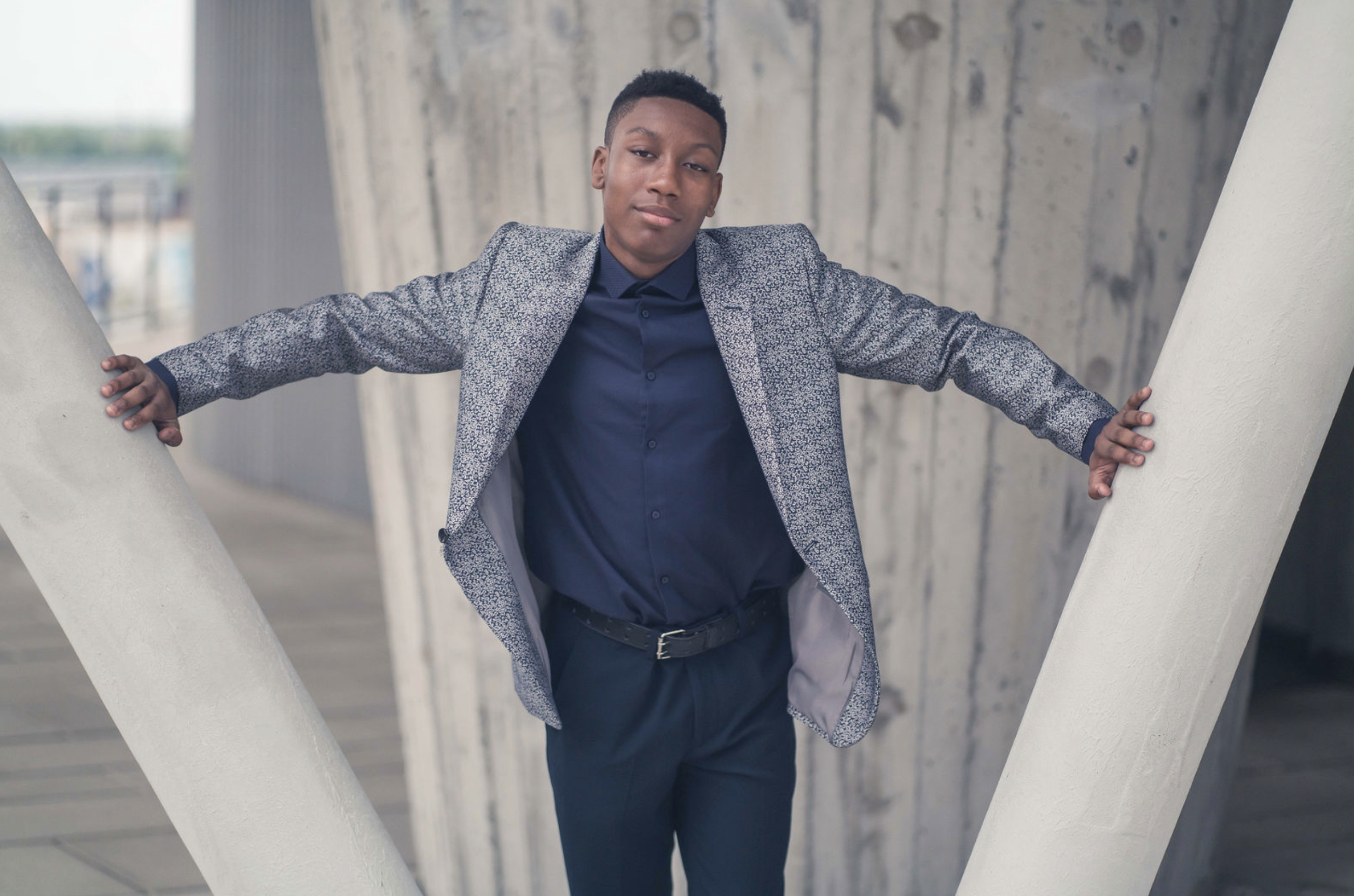 A young man in a patterned jacket standing between architectural columns